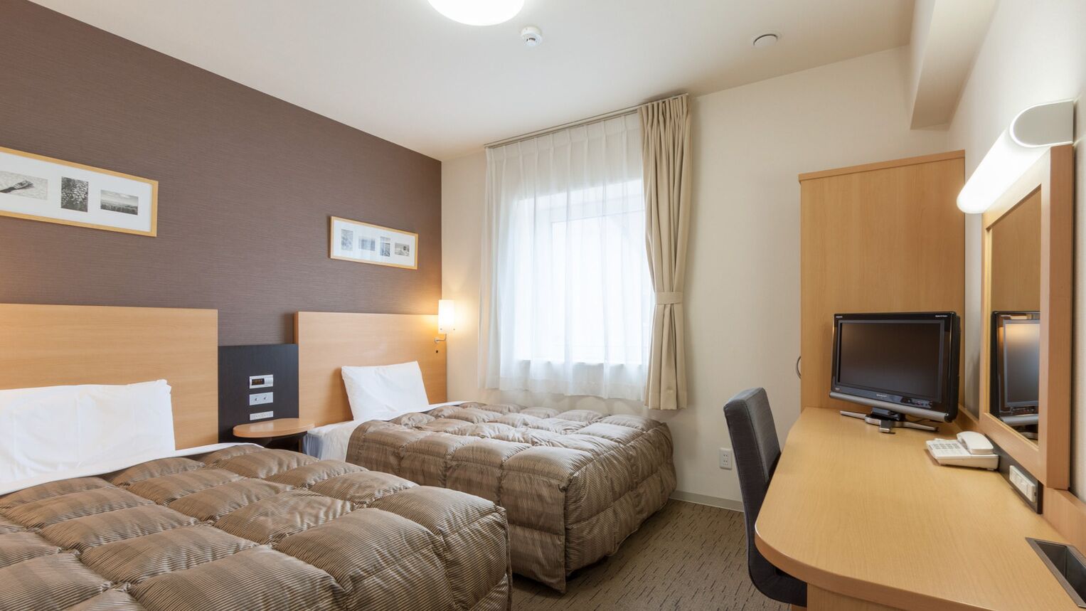 Habitació d'hotel amb dos llits, un escriptori amb televisió i una finestra amb cortines.