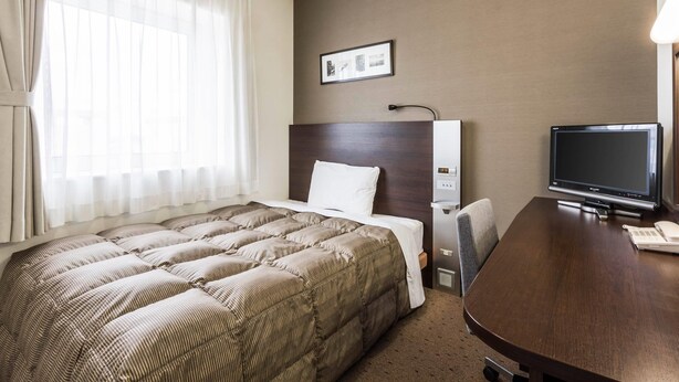 A hotel room with a large bed, a desk with a television, and a window with curtains.