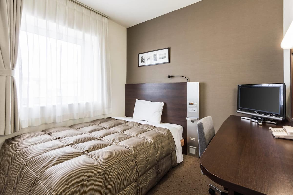 A hotel room with a large bed, a desk with a television, and a window with curtains.