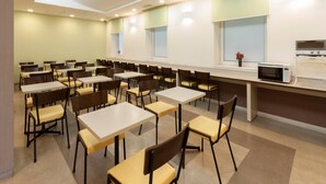 A dining area with multiple tables and chairs, a microwave on a counter, and a window with a view. - Comfort Hotel Kitami (Kitami)