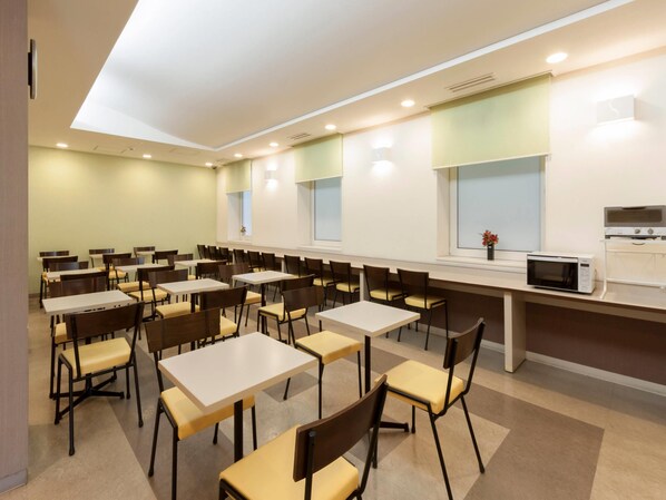 Comedor con varias mesas y sillas, un microondas sobre una encimera y una ventana con vistas.