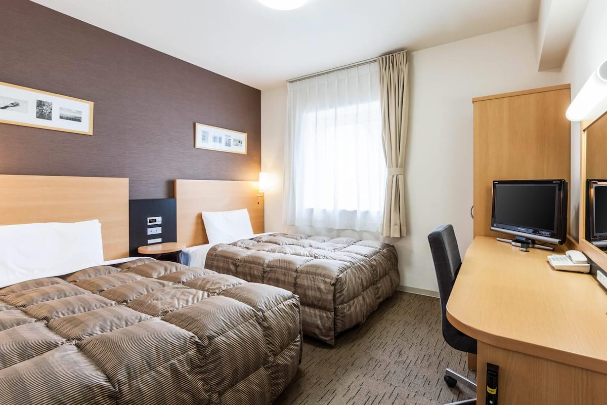 A hotel room with two beds, a desk with a computer, a TV, and a lamp.