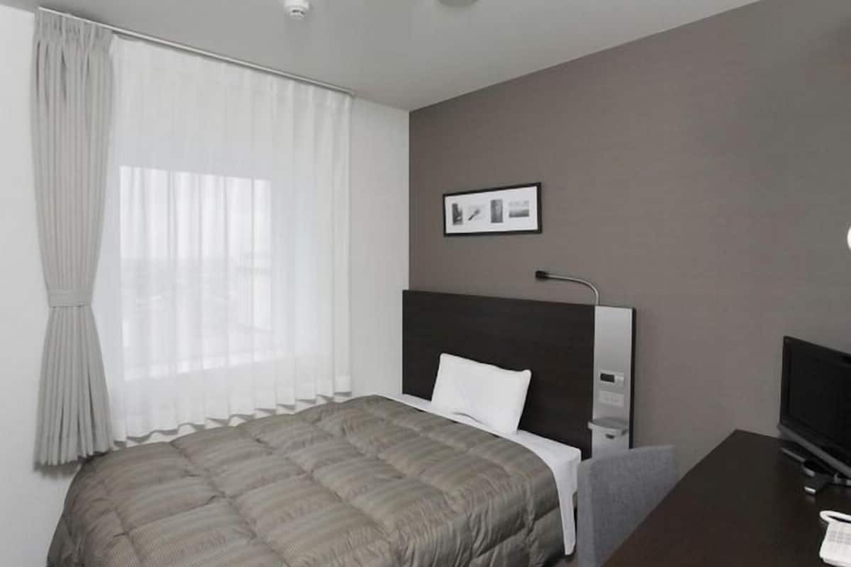 A modern hotel room with a bed, a TV, a desk, and a picture on the wall.