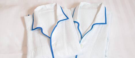 Dos batas blancas ordenadamente dobladas con detalles azules sobre una cama.