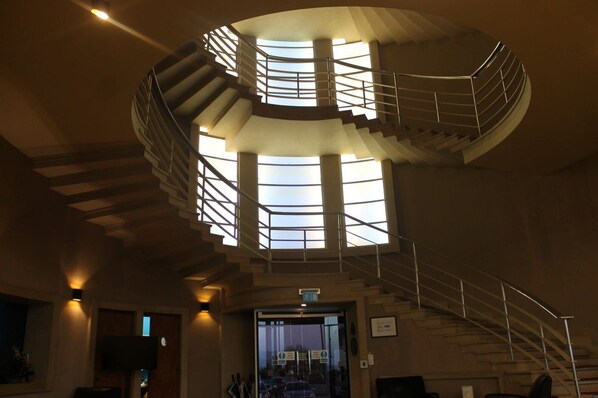 A spiral staircase with a glass enclosure at the top, leading to a landing area with a door and a sign. - The Midland (Morecambe)