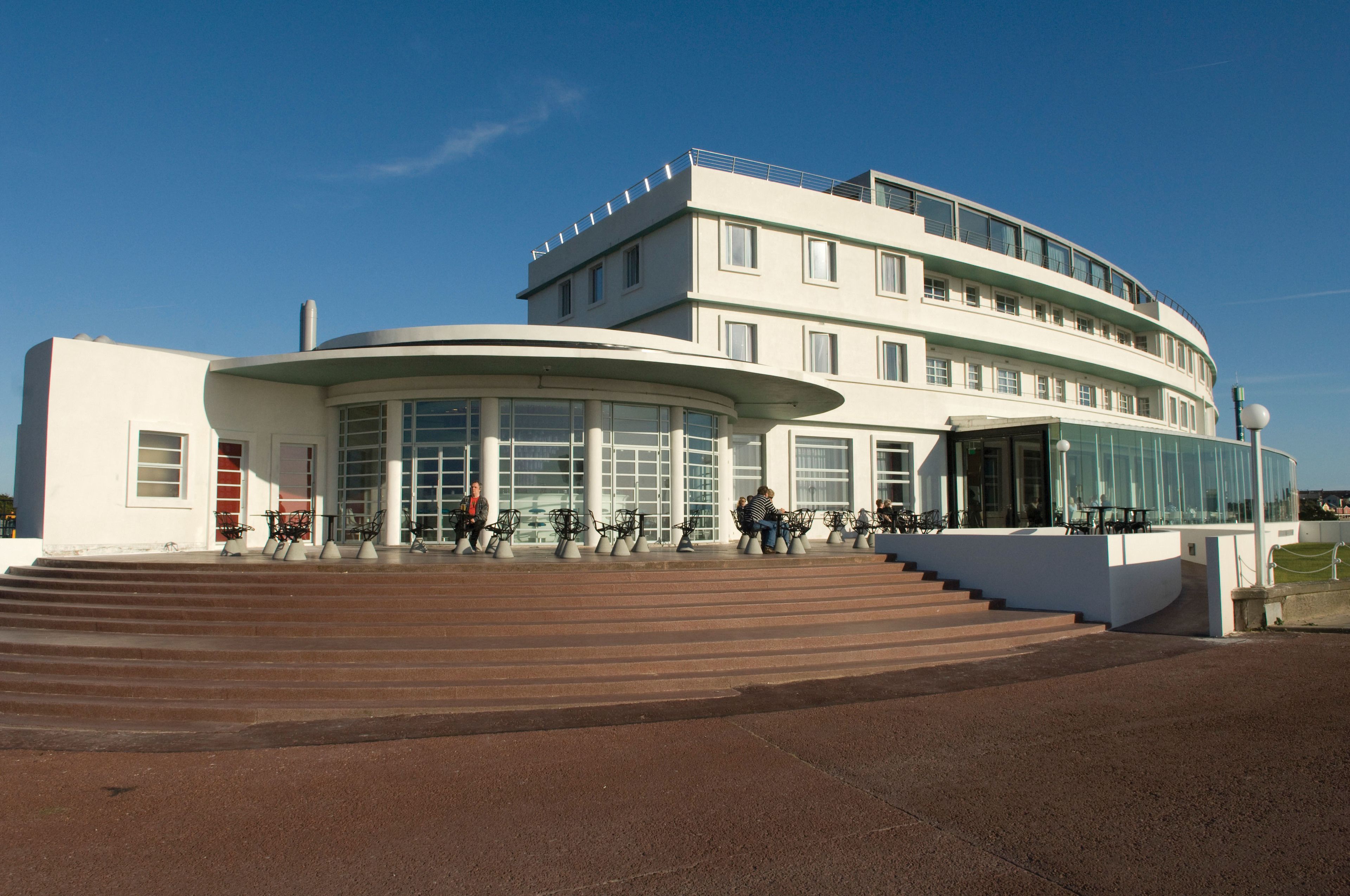 Ein modernes Gebäude mit einer geschwungenen Fassade, großen Fenstern und einer Treppe, die zu einem Eingang führt.