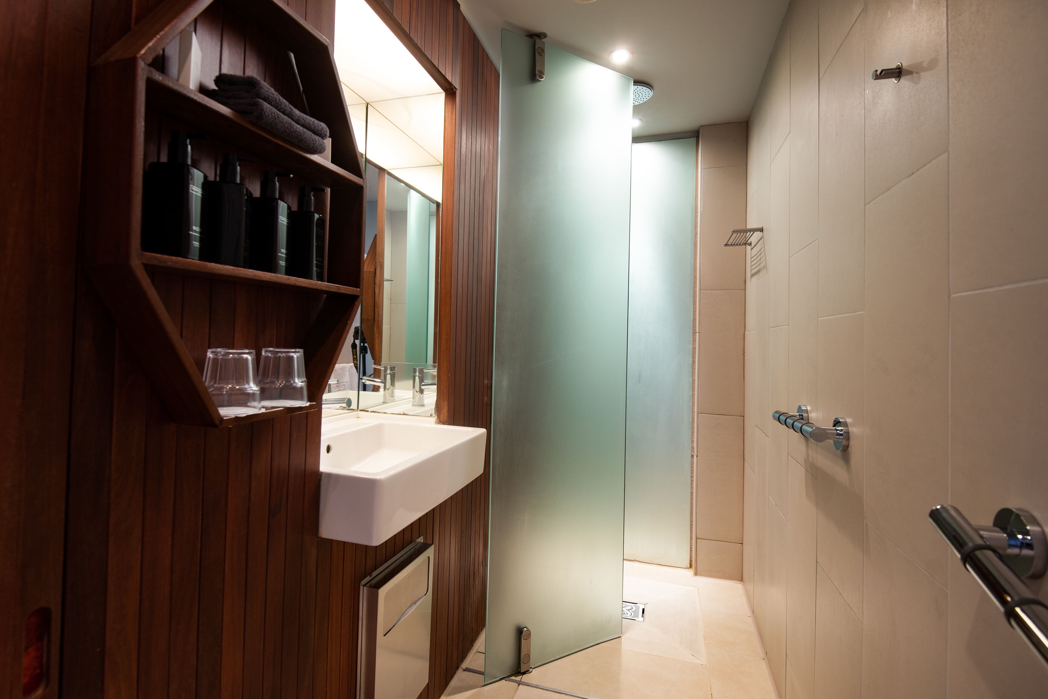 A modern bathroom with a wooden vanity, a white sink, and a glass shower enclosure.