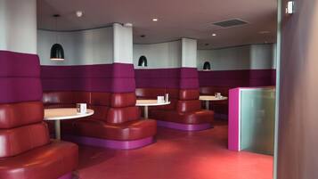Cozy booths surround small round tables, separated by partitions, in a stylish space with pendant lights and a bold red floor.