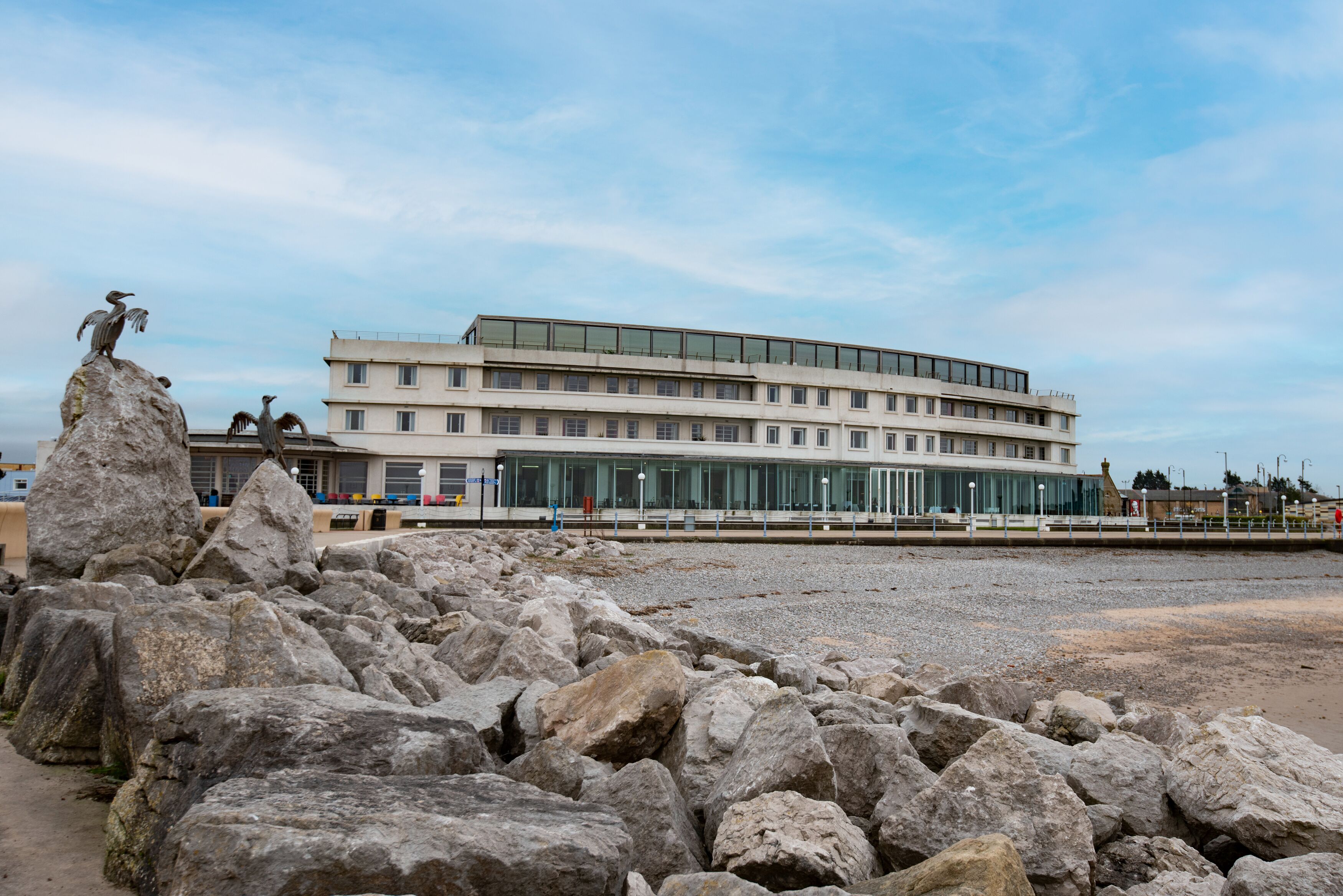 A coastal building with a modern design, large windows, and a rocky foreground.