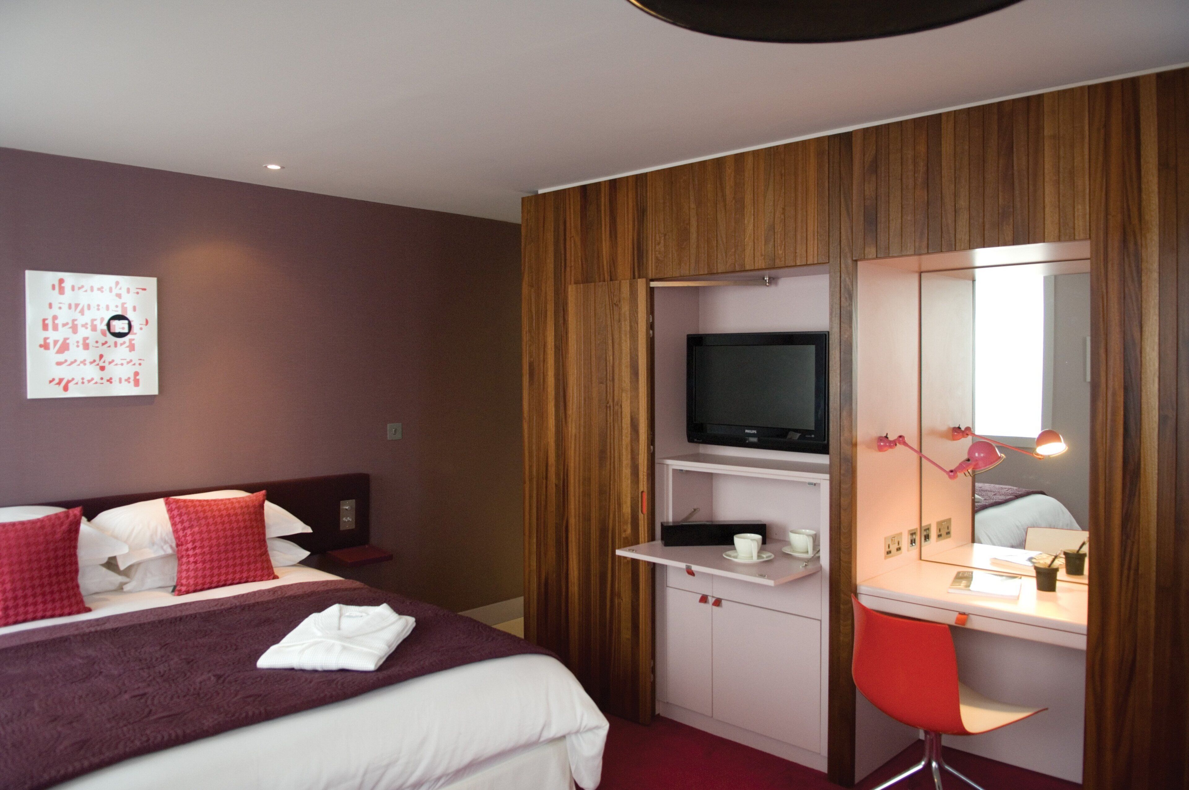 A hotel room with a bed, a desk with a computer, a TV, and a mirror.