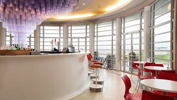 Zona de bar moderna con una barra curva, taburetes rojos y ventanas amplias con vistas al exterior.