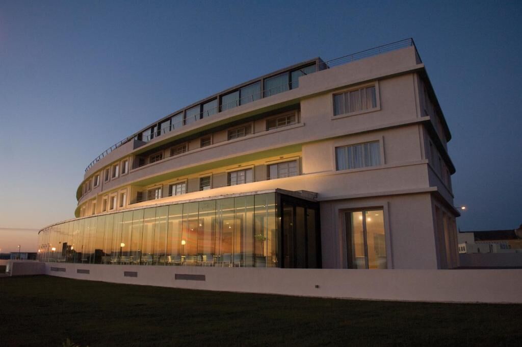 A modern hotel with a curved facade, large glass windows, and multiple balconies.