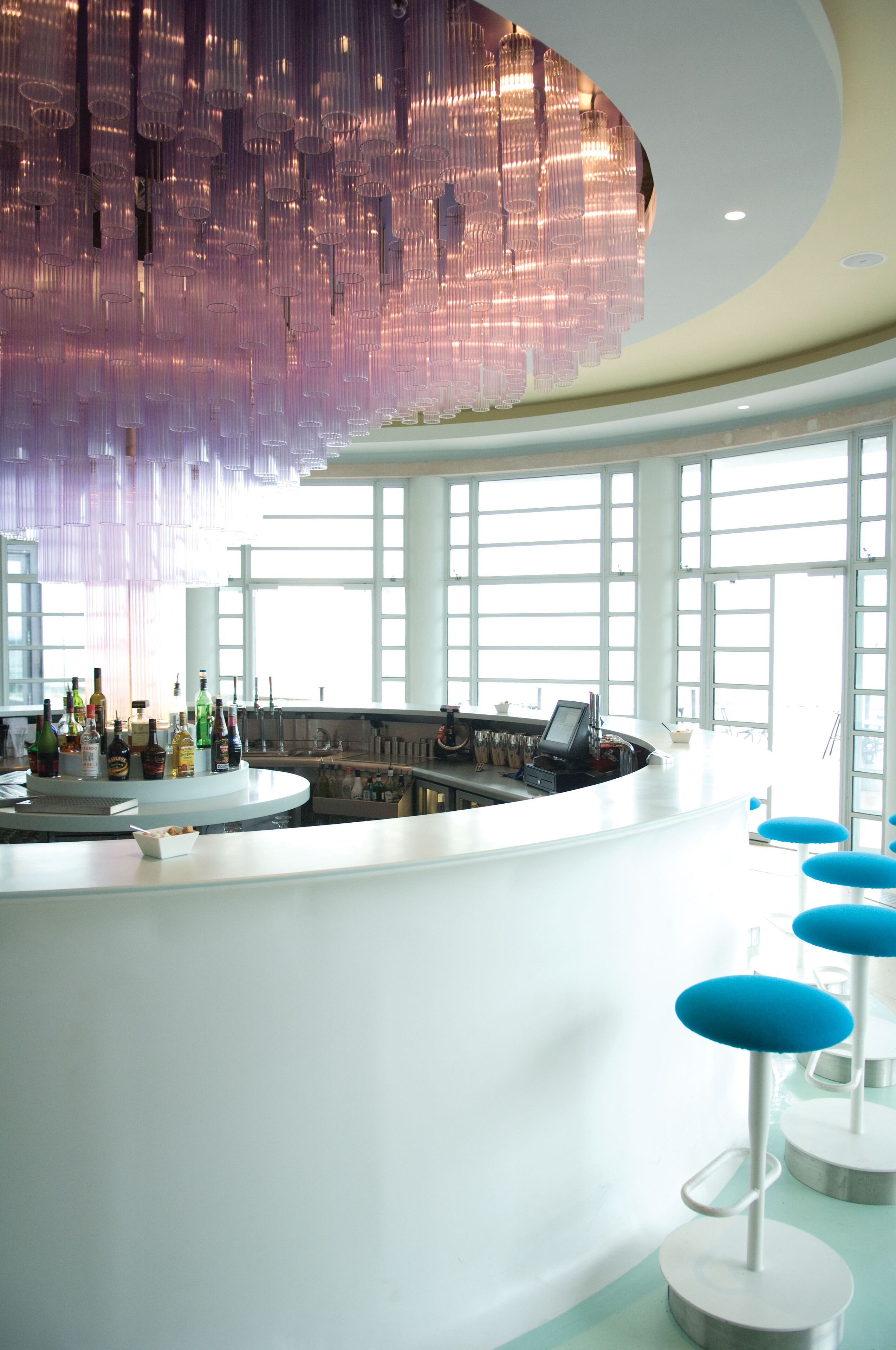 A modern bar area with a circular counter, bar stools, and a decorative hanging light fixture.