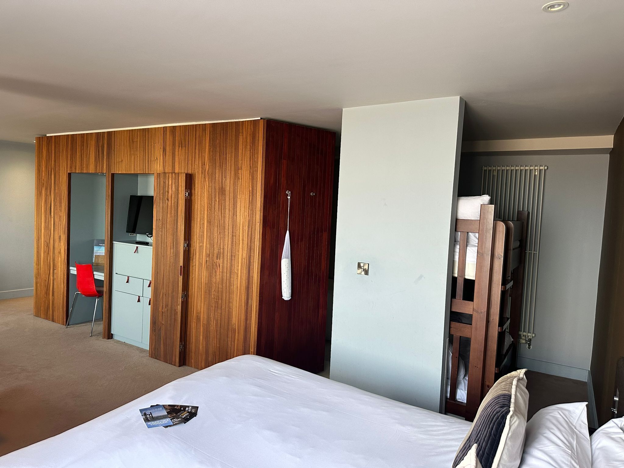 Una habitación de hotel con cama, escritorio y silla, armario y radiador.