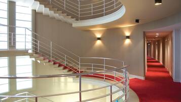 A modern hotel interior with a spiral staircase, a red carpeted corridor, and wall-mounted lighting.