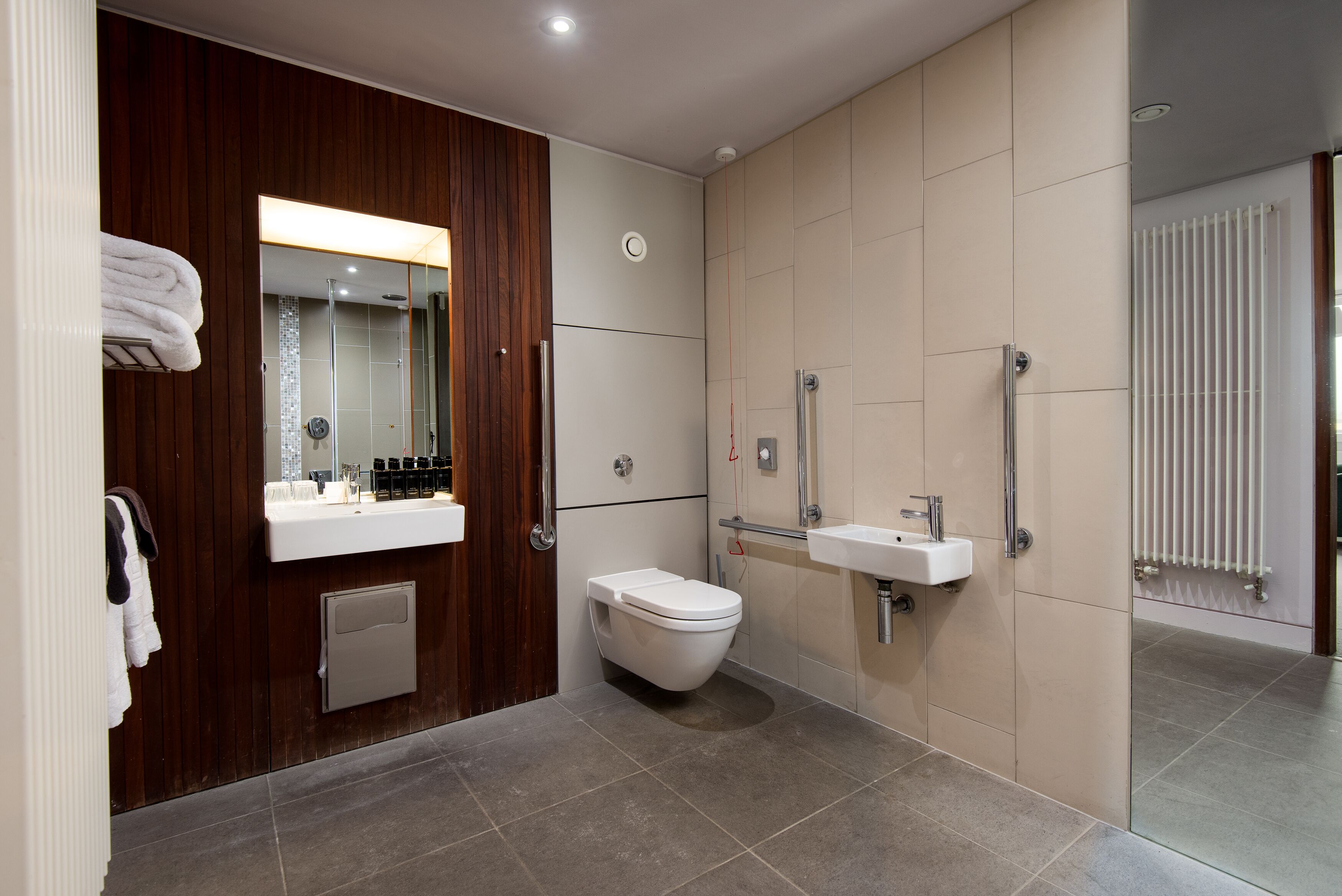 Un baño moderno con tocador de madera, inodoro, lavamanos y zona de ducha.