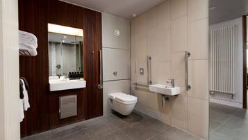 Un baño moderno con tocador de madera, inodoro, lavamanos y zona de ducha.