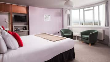 Habitación de hotel con una cama grande, televisión, una mesita, dos sillas y ventana con vistas.
