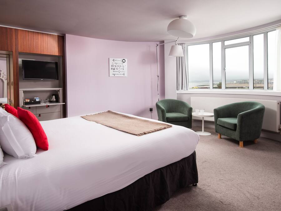 Habitación de hotel con una cama grande, televisión, una mesita, dos sillas y ventana con vistas.