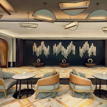 A modern lounge area with contemporary furniture, a patterned carpet, and a decorative wall with vertical elements.