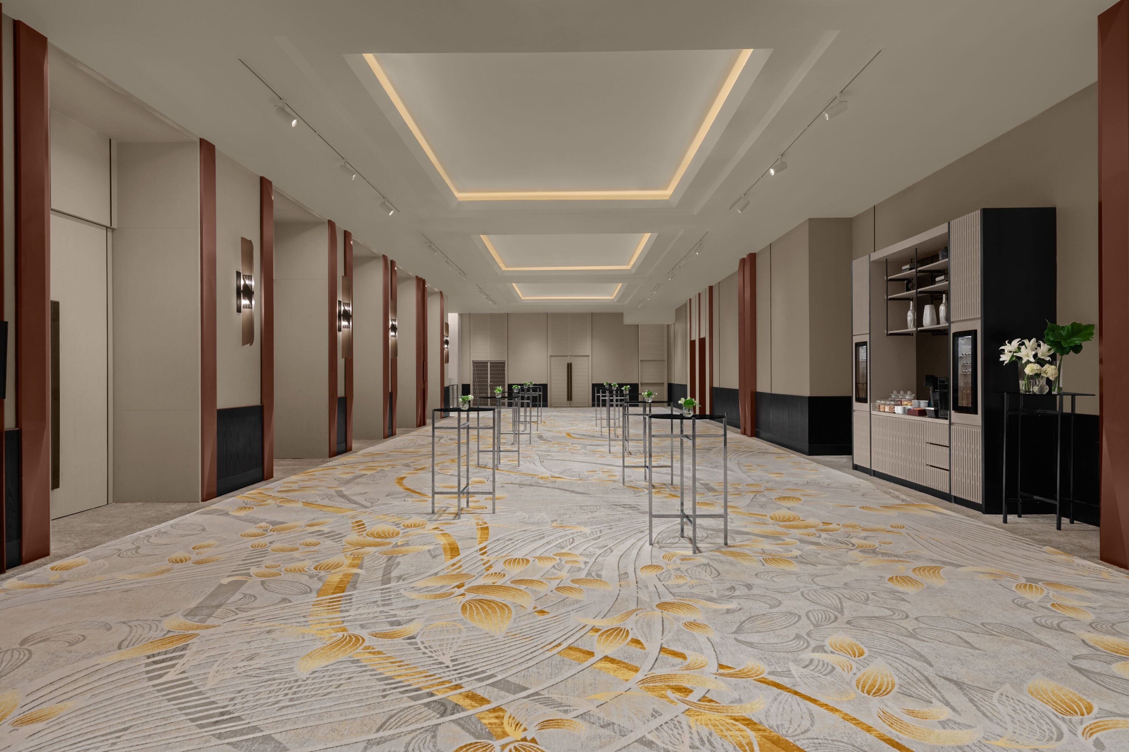 A spacious hotel lobby with a patterned carpet, modern lighting, and a reception area.