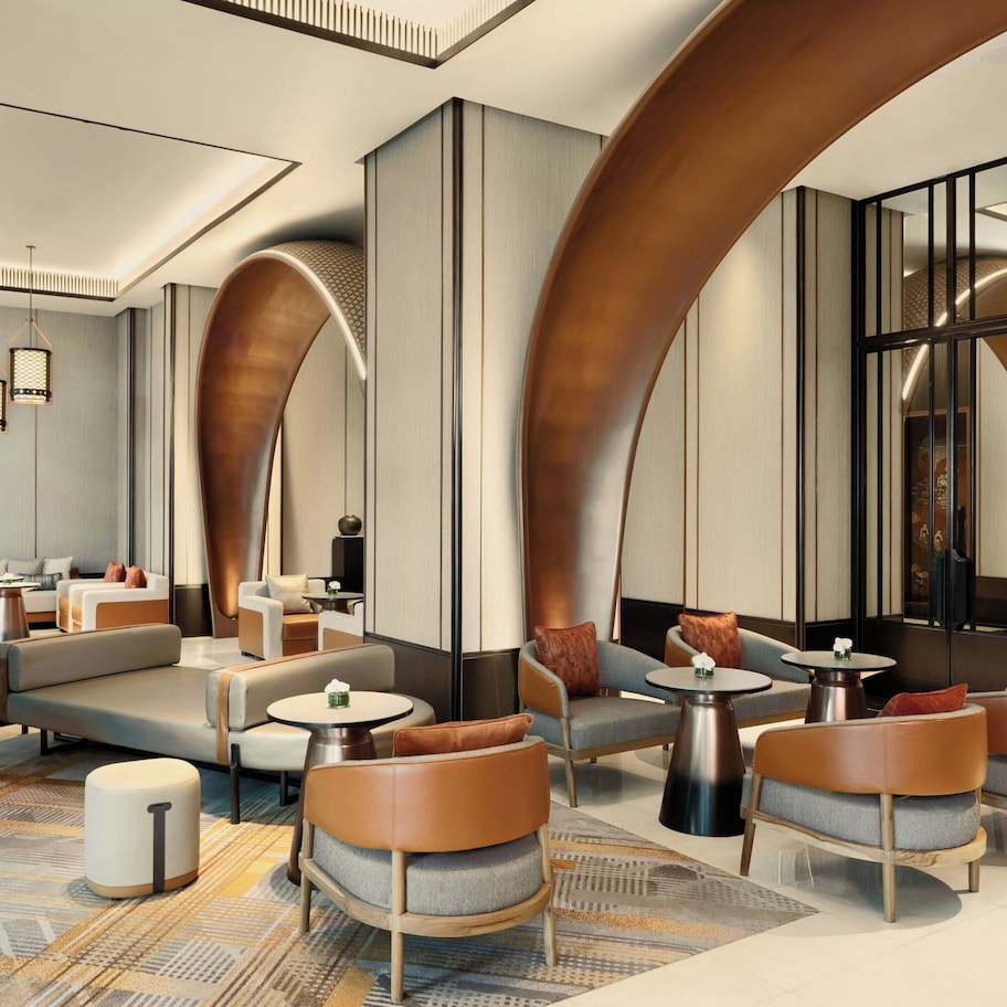 A modern hotel lobby with a seating area, large windows, and a decorative archway.