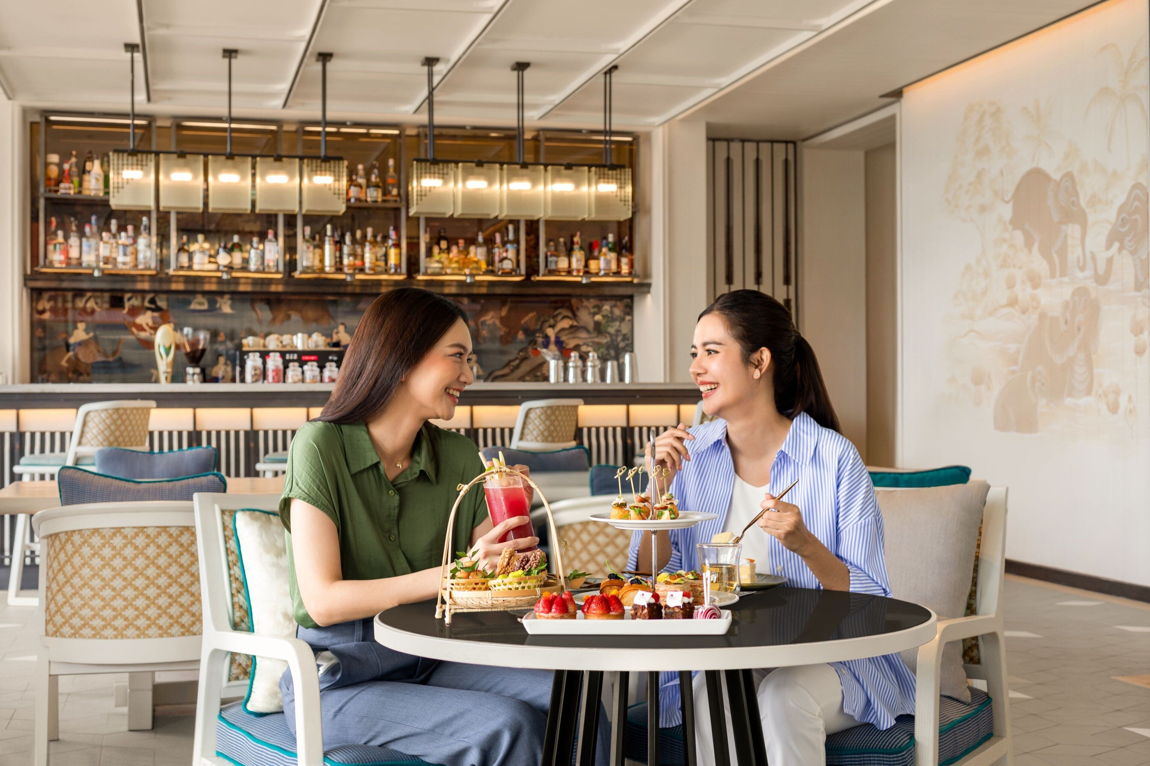 A dining area with a bar in the background, featuring a variety of bottles and a mural.
