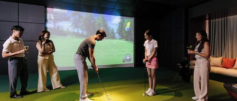 A group of people on a golf course simulation with a large screen displaying the game.