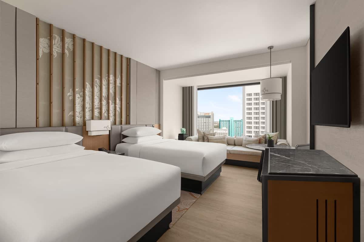 A hotel room with two beds, a desk, a TV, and a city view.