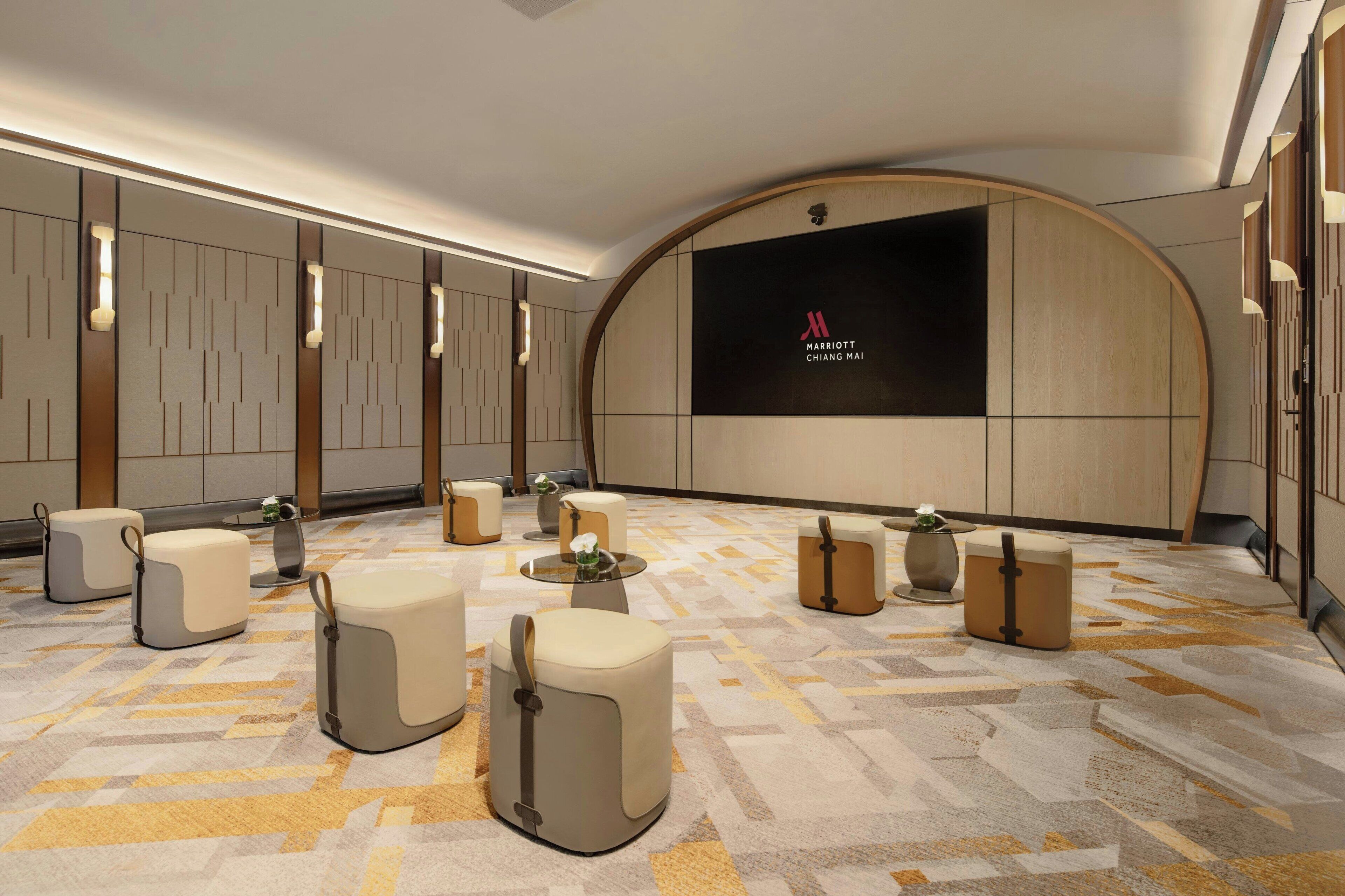Un moderno vestíbulo de hotel con una pantalla grande mostrando el logotipo de Marriott, varias zonas de estar y una alfombra estampada.