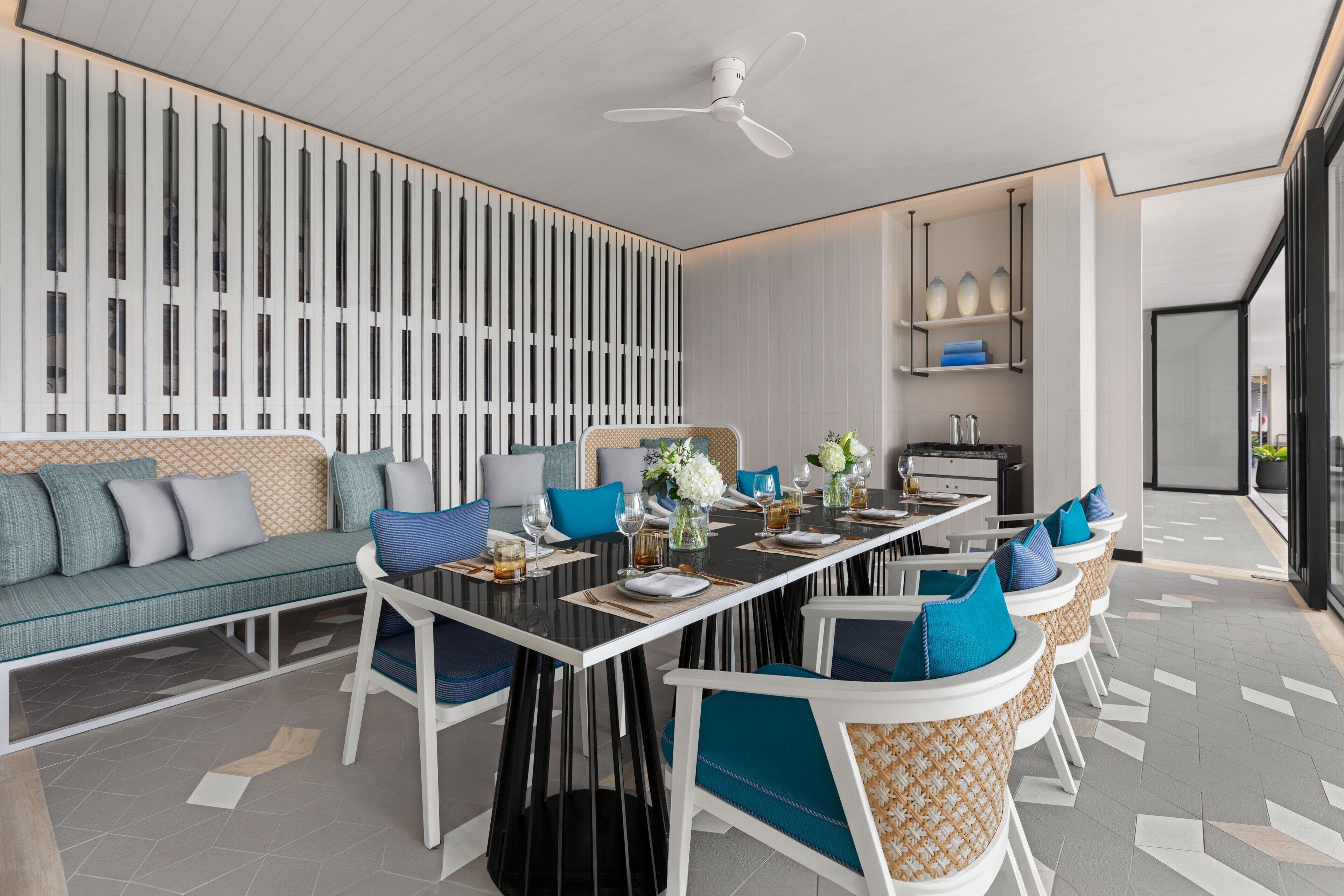 A modern dining area with a long table, white chairs, and a ceiling fan.