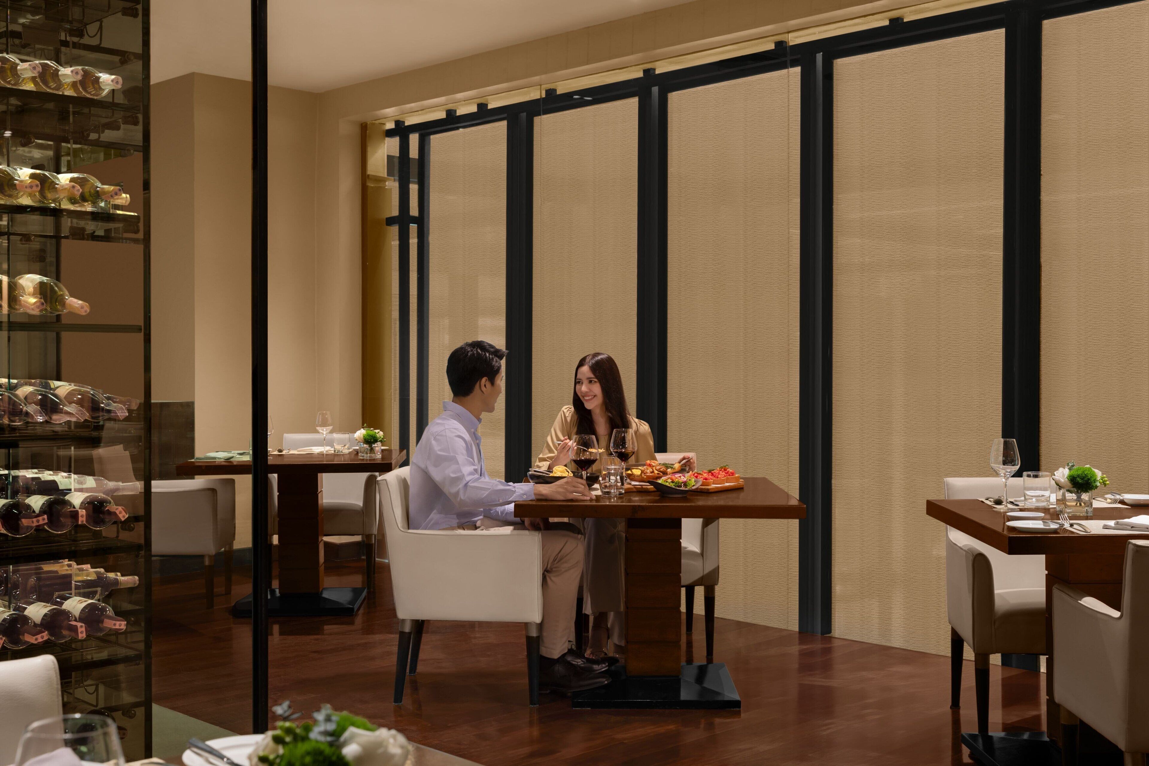 A dining area with a table set for two, a wine rack, and a view through a partition.