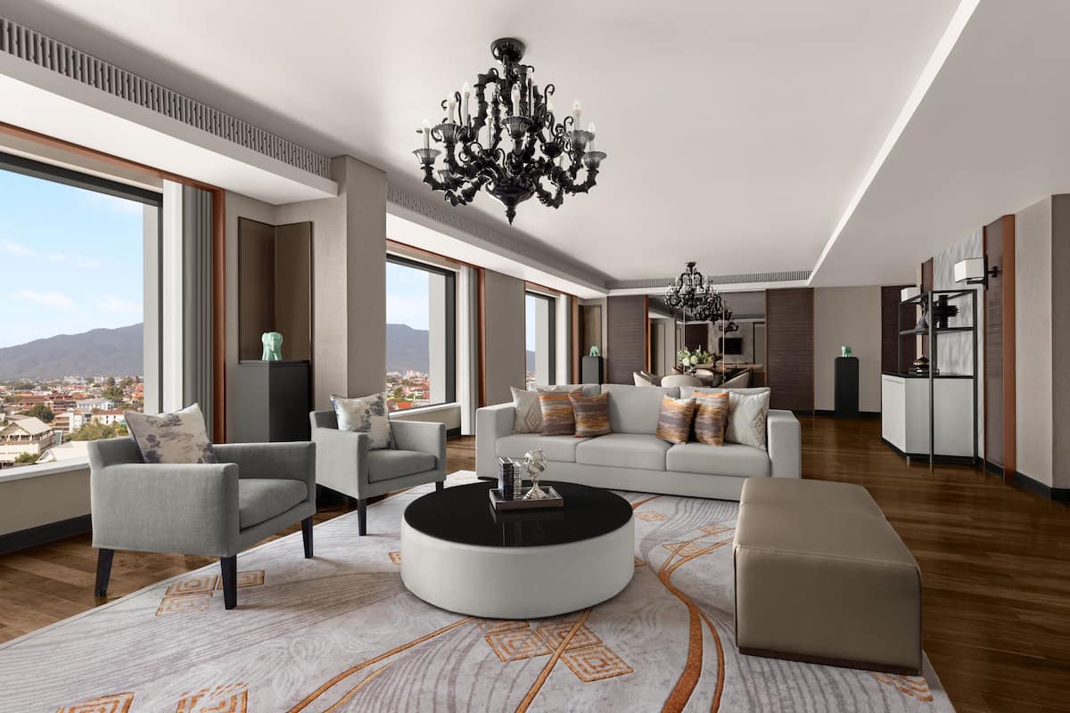 A spacious living room with a large window, a round coffee table, and a chandelier.