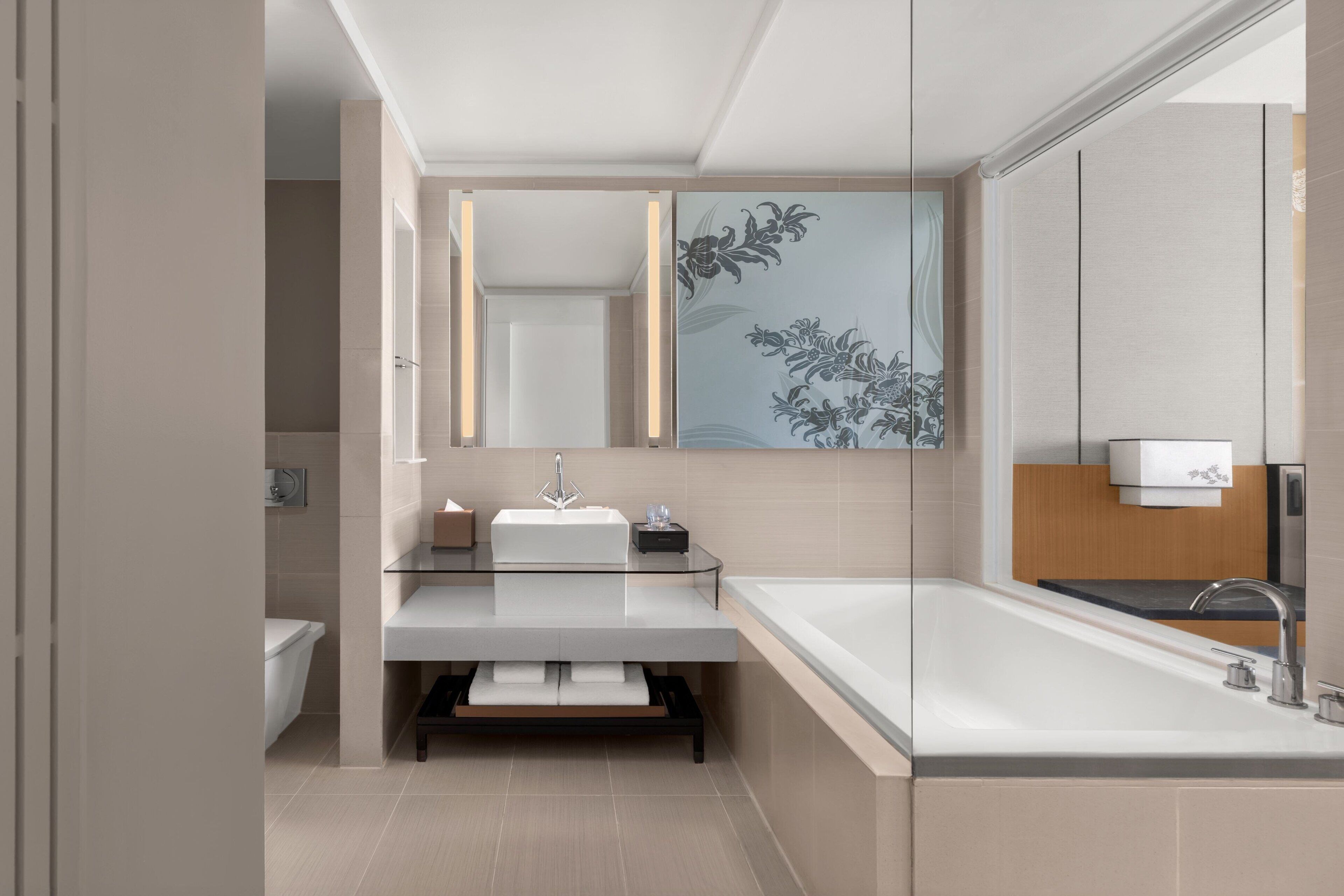 A modern bathroom with a glass vanity, a large mirror, and a bathtub.