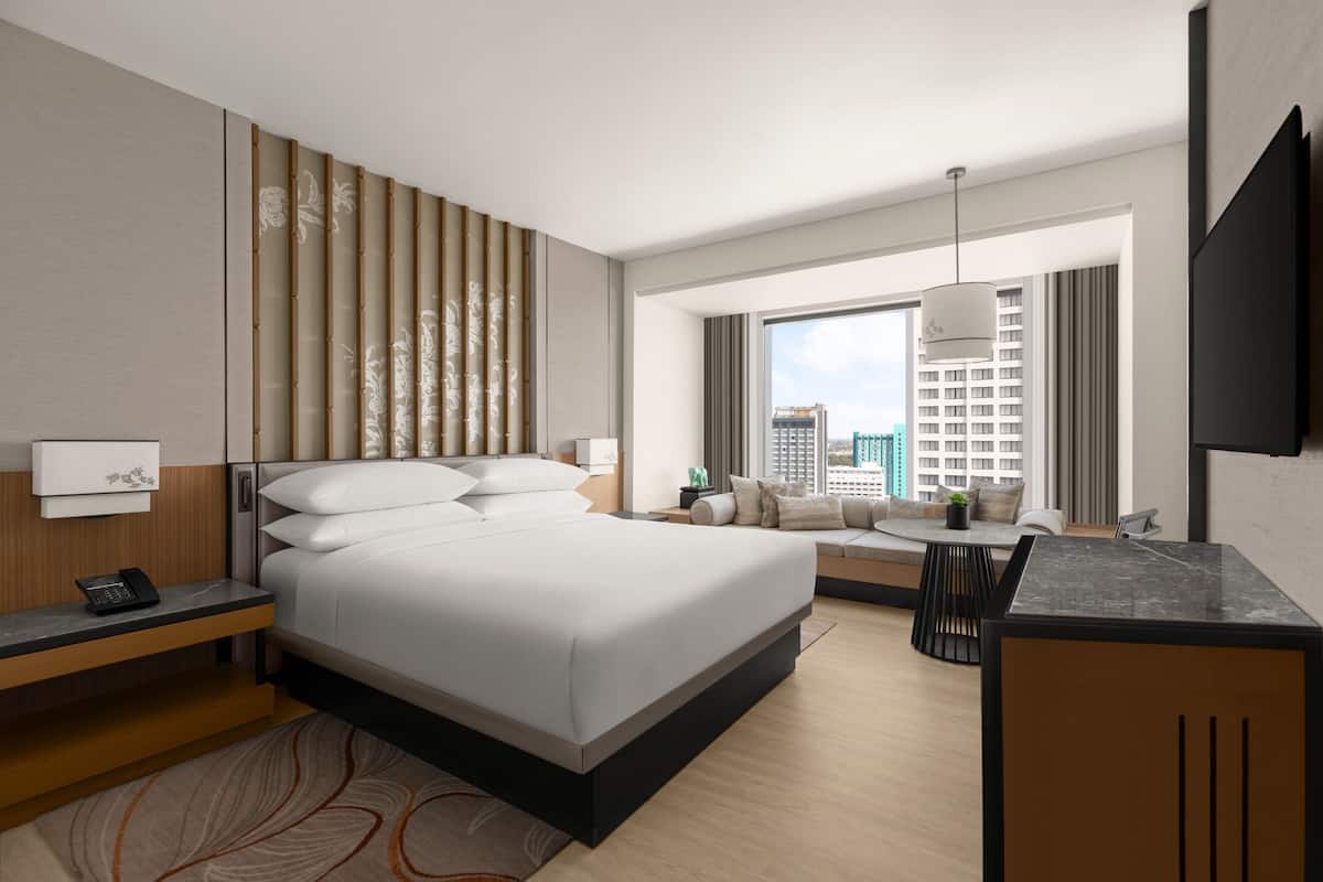 A modern hotel room with a large bed, a desk, a sofa, and a city view.