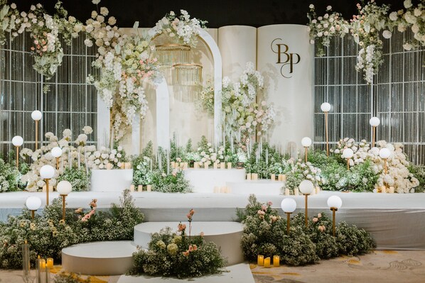 Un escenario con arreglos florales y una araña, con un fondo que muestra el logotipo 'BP'.