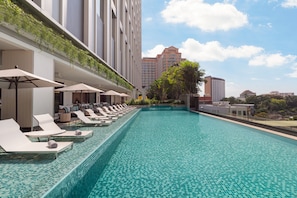 Relax by the rooftop infinity pool, surrounded by lounge chairs and umbrellas, with a stunning city view.