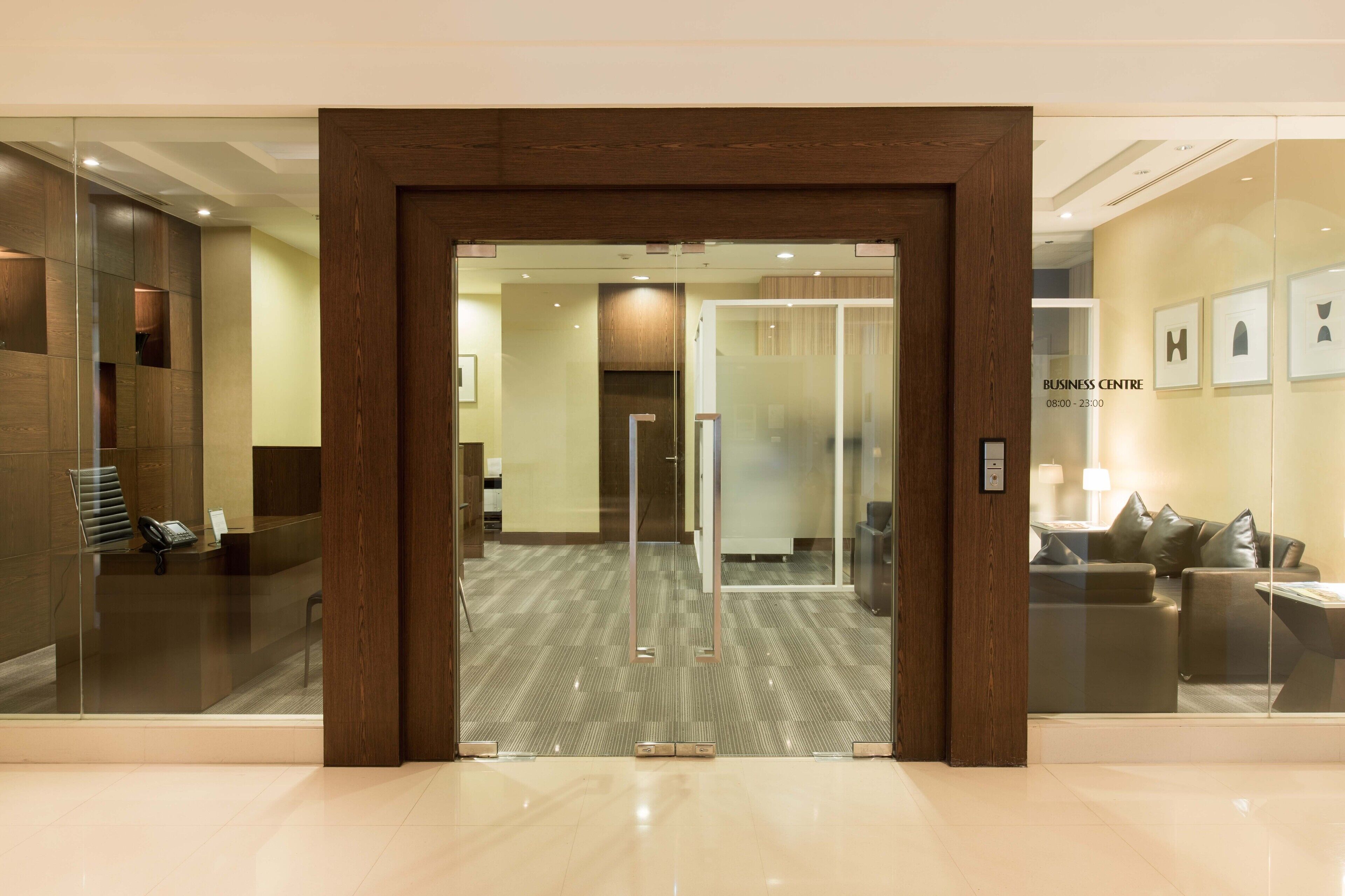 A modern business center with a reception desk, glass doors, and a seating area with a sofa and lamp.