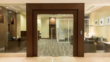 A modern business center with a reception desk, glass doors, and a seating area with a sofa and lamp.