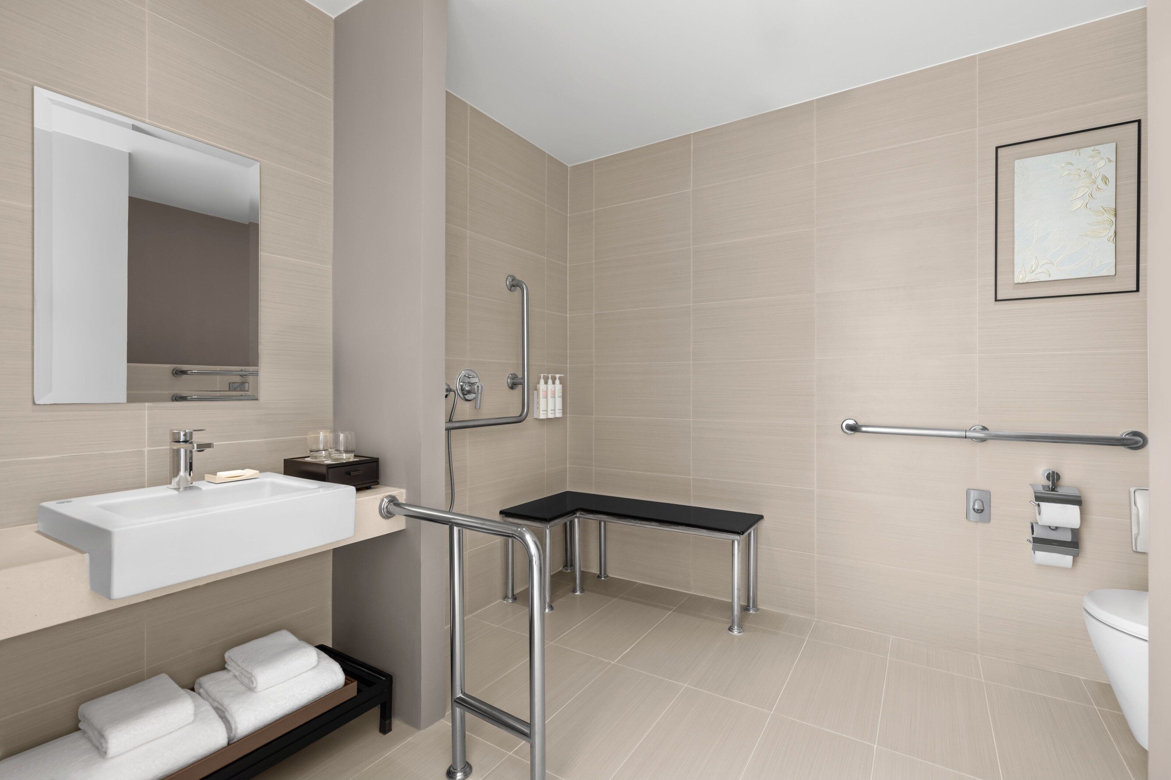 A modern bathroom with a sink, mirror, towel rack, shower, and toilet.