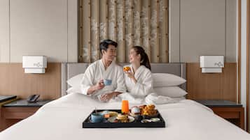 A hotel room with a bed, bedside tables, a phone, and a tray with breakfast items.
