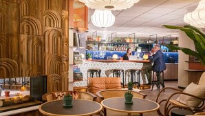 A bar area with a counter, stools, and a seating area with round tables and chairs. - Novotel Suites Nice Airport (Nice)