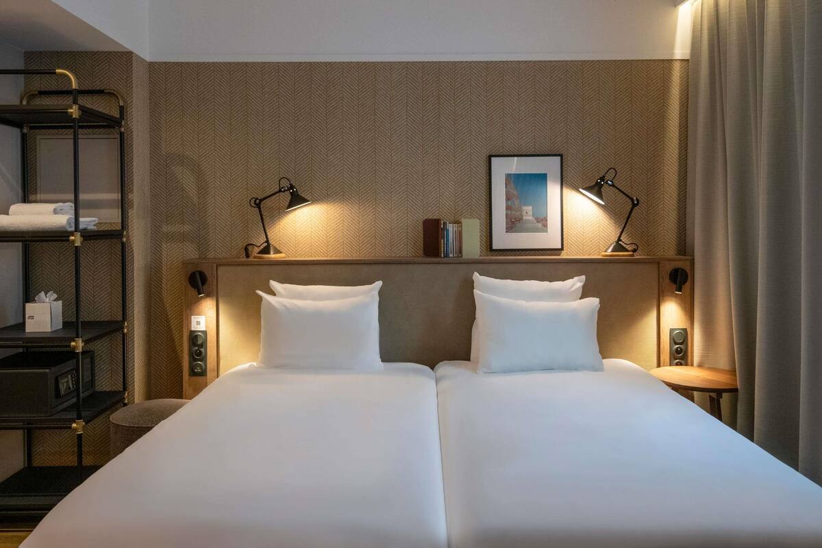 A double bed with two bedside tables, a shelf with towels, and a framed picture on the wall.