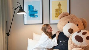 A bed with a large teddy bear, a framed picture of a building, and a floor lamp. - Novotel Suites Nice Airport (Nice)