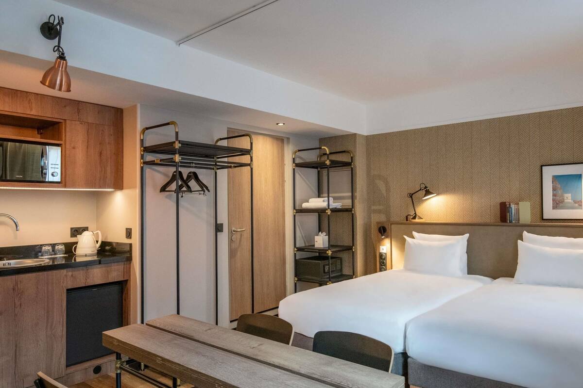 A hotel room with a bed, a desk, a chair, a small kitchenette, and a wardrobe.
