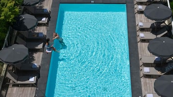 Una piscina rectangular con agua cristalina, rodeada de tumbonas y sombrillas.
