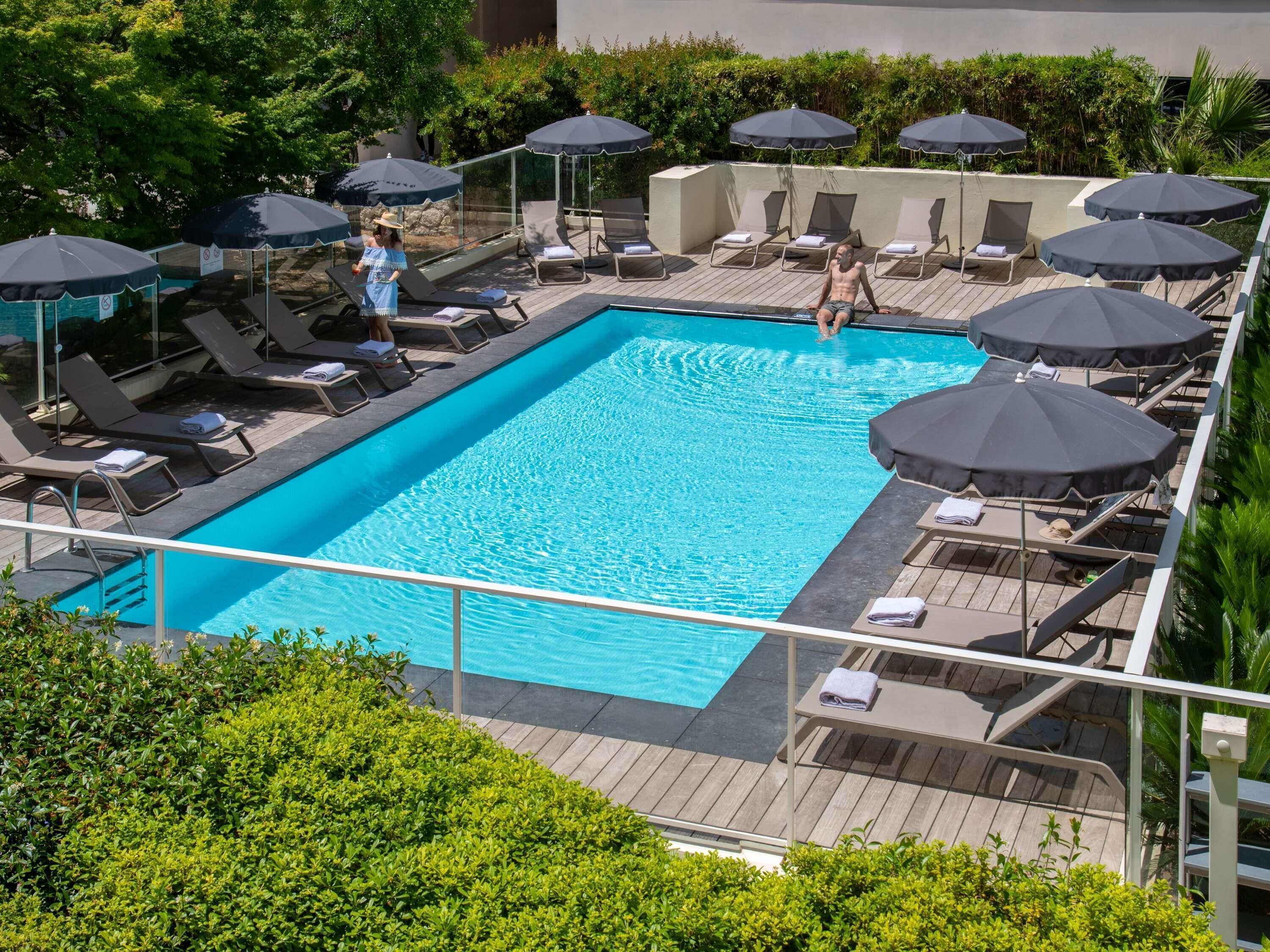 A rectangular pool with lounge chairs and umbrellas, surrounded by greenery.
