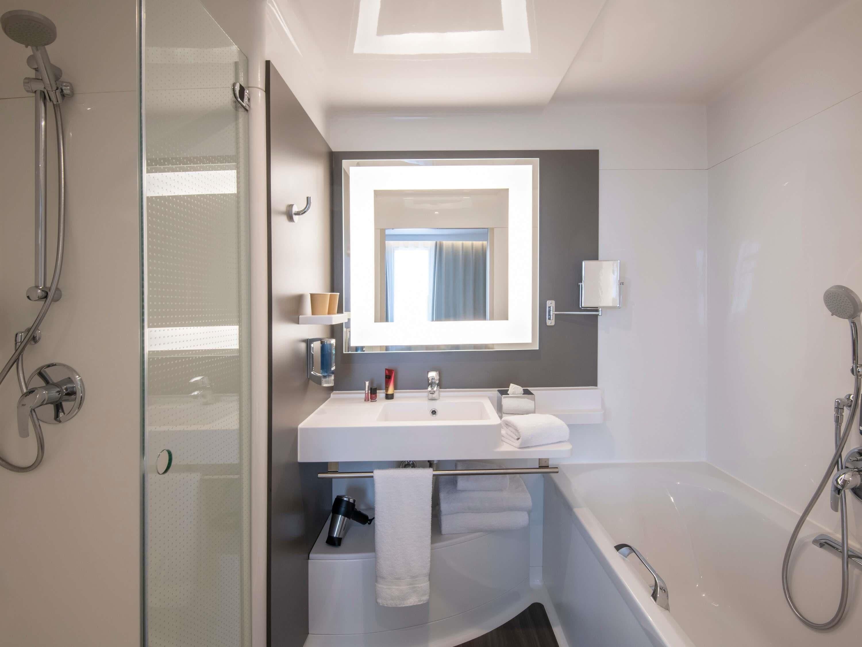 Une salle de bain moderne avec une douche à parois de verre, un lavabo blanc, un miroir et une baignoire.