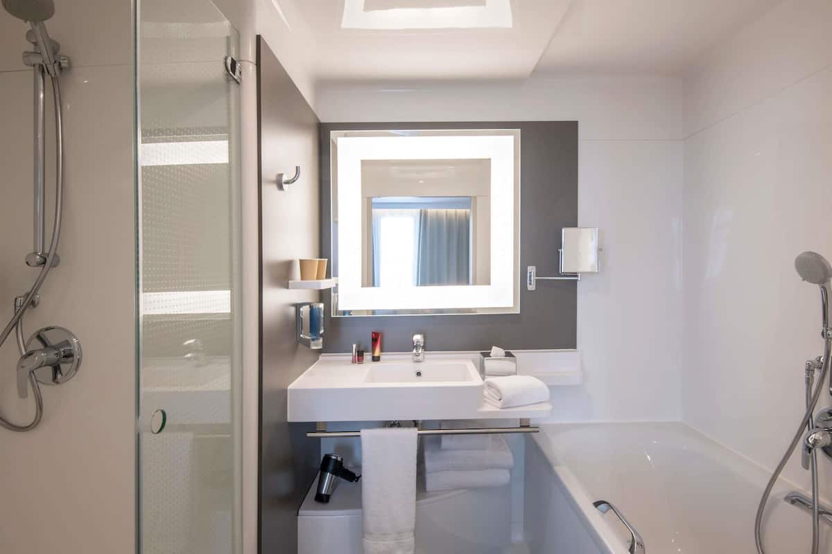 Une salle de bain moderne avec une douche Ă parois de verre, un lavabo blanc, un miroir et une baignoire.