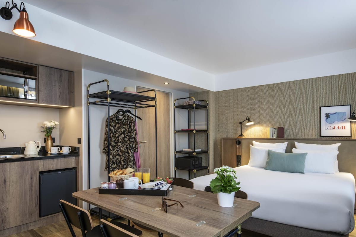 Una habitación de hotel compacta con cama, mesita de noche y una pequeña kitchenette.